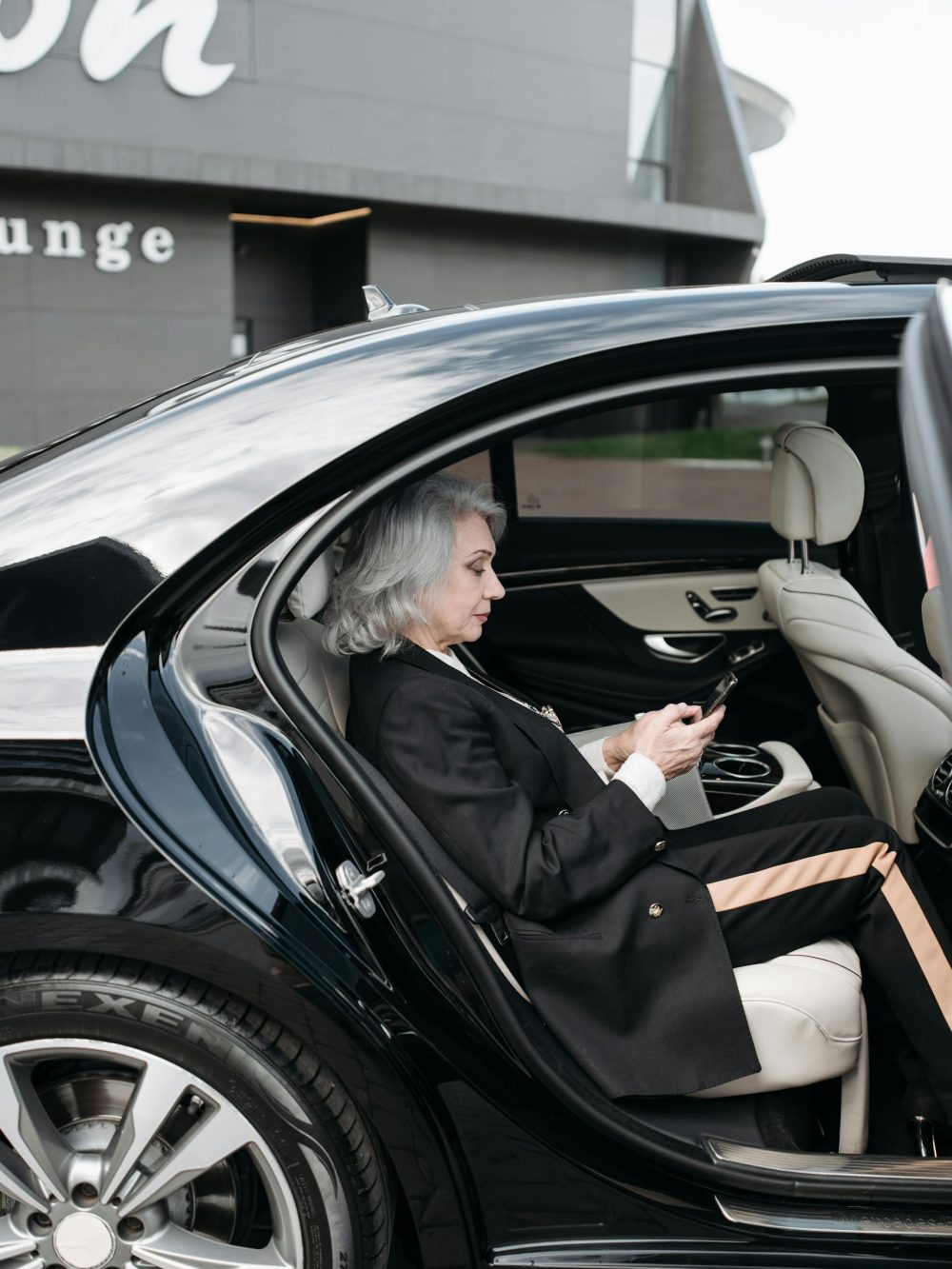 senior-woman-in-business-attire-sits-in-a-luxury-car-using-a-tablet-outside-a-modern-building.-8424931-scaled